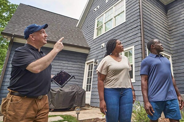 A contractor and two homeowners inspect the outside of their home