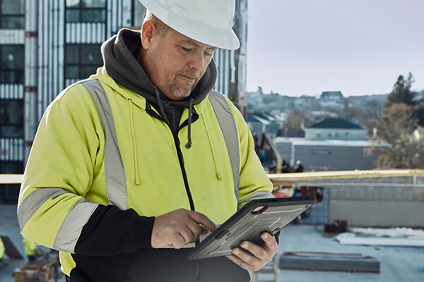 Commercial roofing contractor on top of flat roof using GAF services on tablet