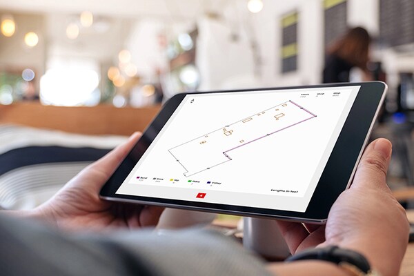 Hands holding a tablet open to QuickMeasure roof measurement app showing a commercial building
